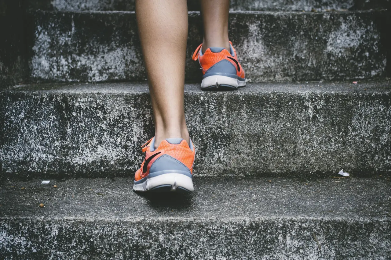 Piernas de una persona con zapatillas deportivas subiendo escalones de piedra